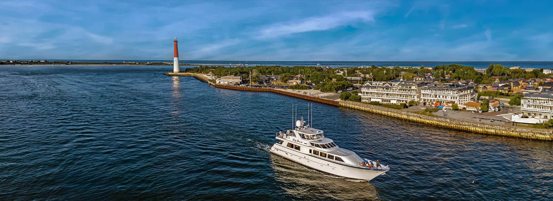 White yacht named Lady Grace cruising on the water with red and white lighthouse in the background