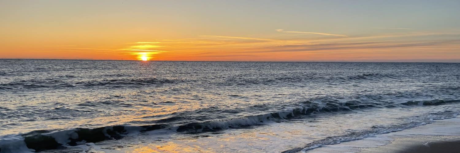 Soft waves rolling onto a beach with setting sun in the background