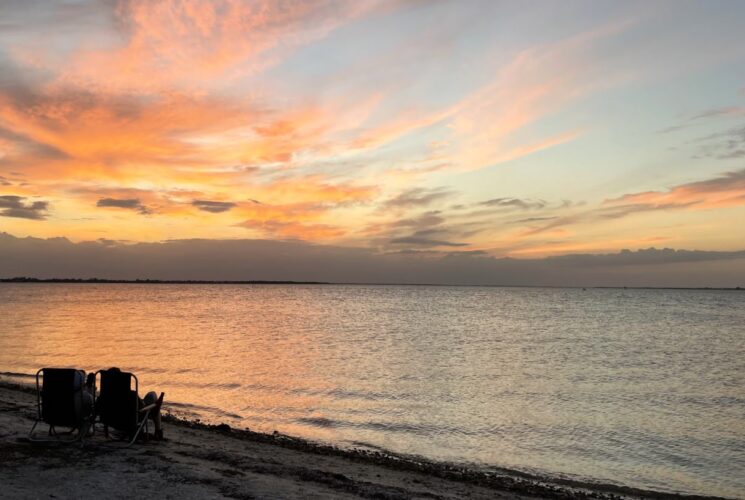 Two people sitting in chairs on the beach with setting sun in the background