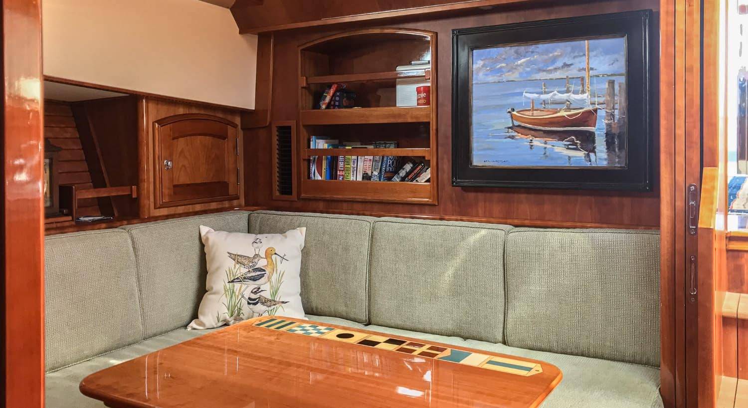 Dining area of motor sailing yacht with dark wood, light green upholstered cushions and wooden table