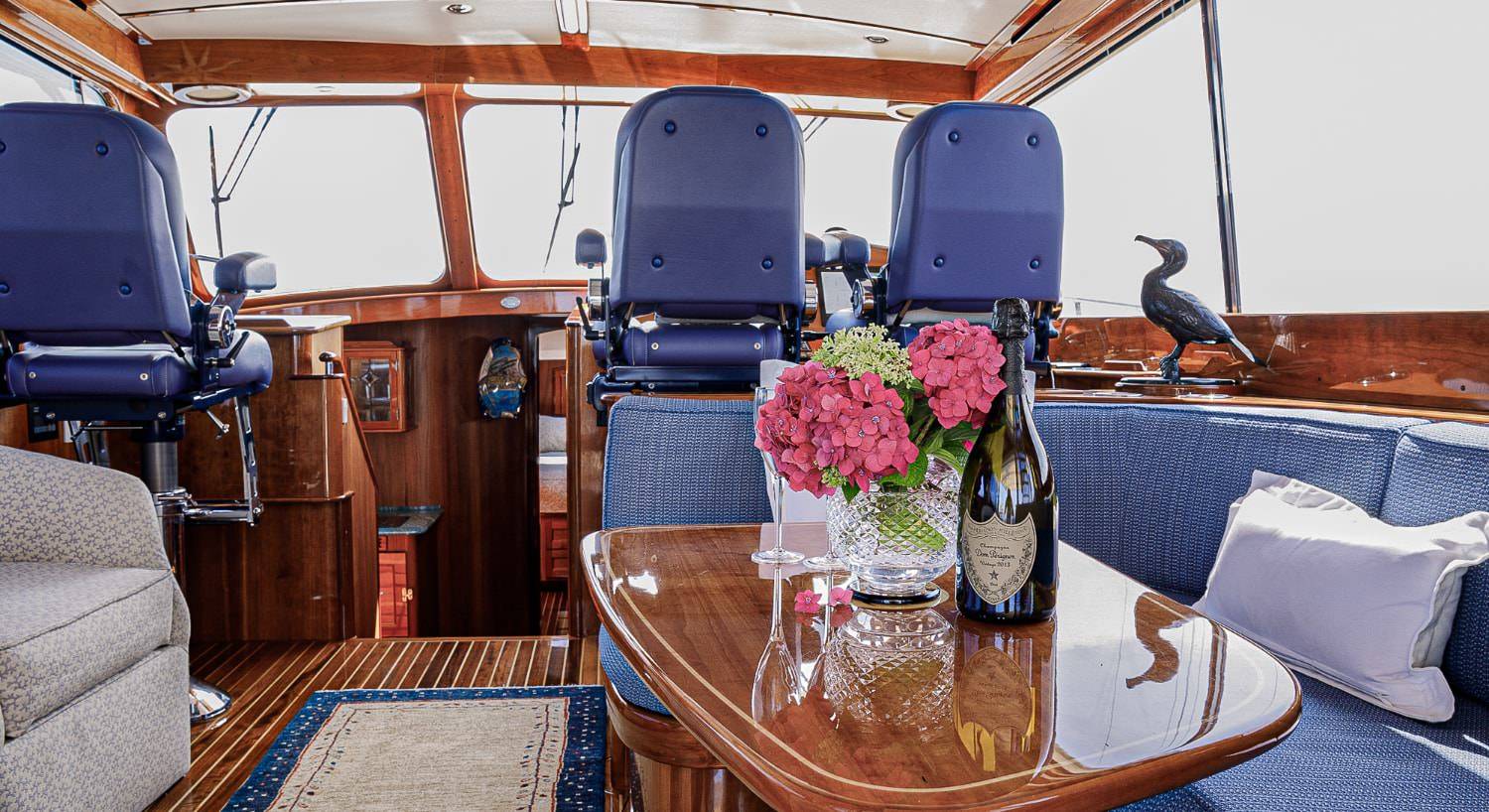 Bridge with dark wood interior, two blue seats, and sitting area with blue upholstered cushions on a sailing motor yacht